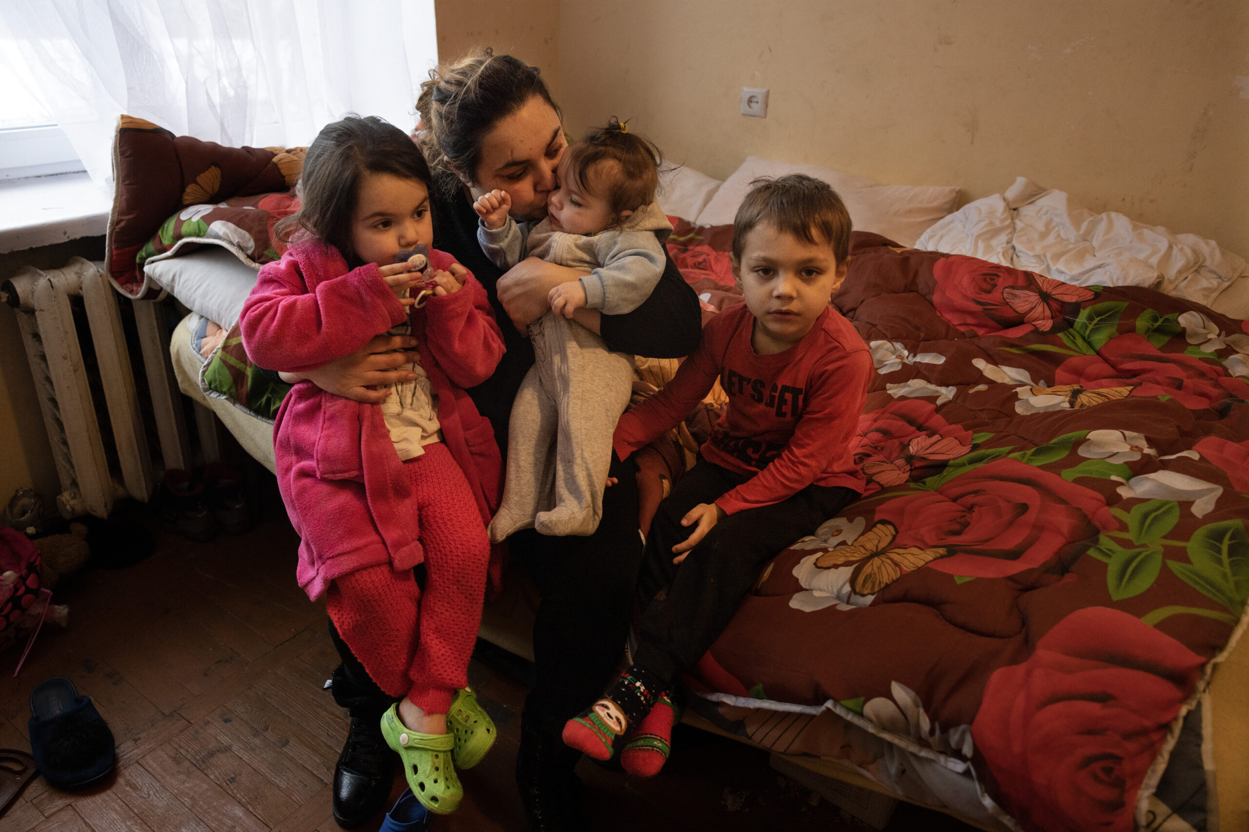 LVIV,UKRAINE - Olena, a mother from Mariupol, Ukraine, holds her children Veronica, 3, Renat, 5, and baby Boghdan, 7 months, inside their small room in a shelter where they have been living for several months after fleeing their now-destroyed city. Olena wishes to relocate to Poland, but she is unable to leave with her current partner as they are not married. Picture taken on February 11, 2023.